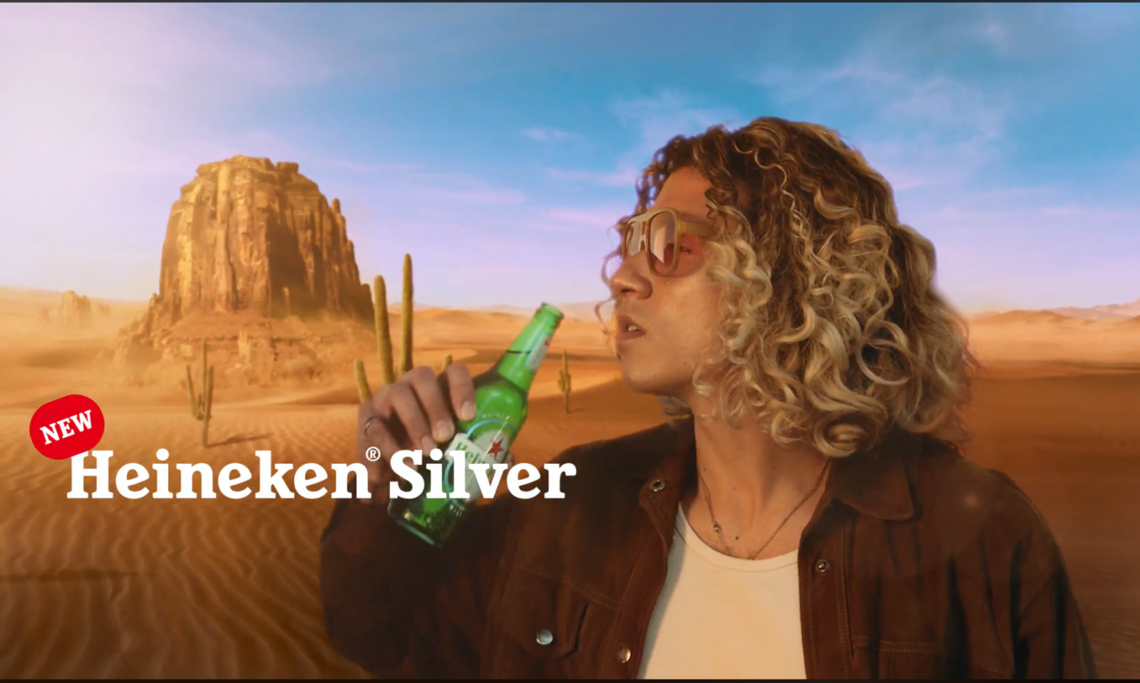Man met zonnebril drinkt Heineken Silver in een woestijnlandschap.