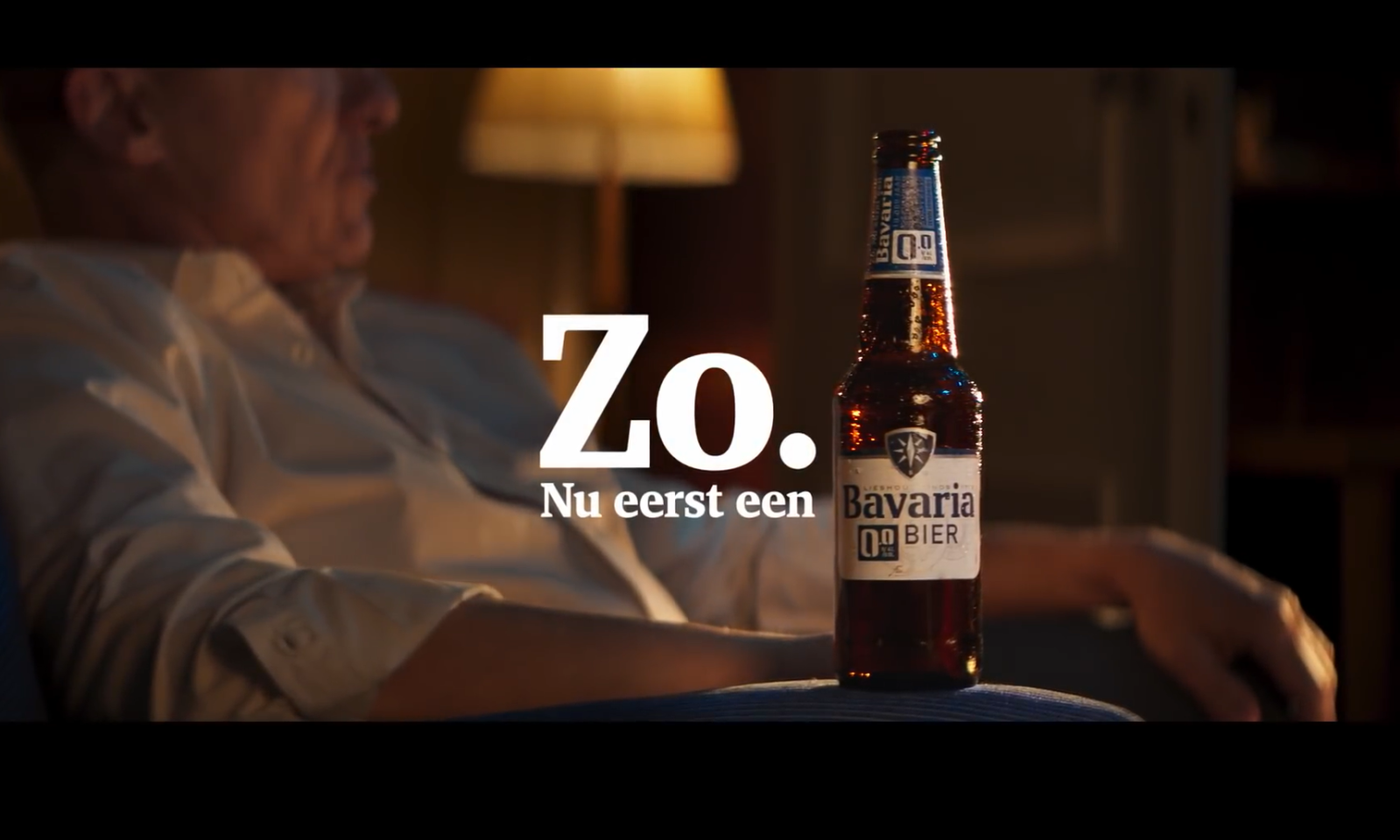 Man in stoel met een fles Bavaria 0.0% bier en tekst 'Zo. Nu eerst een'.