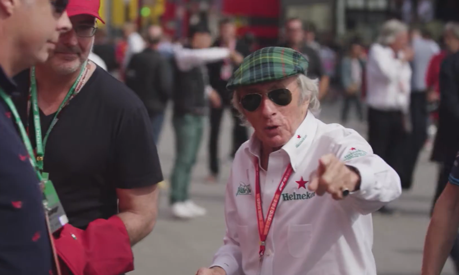 Mensen in gesprek tijdens een Formule 1 evenement, een persoon met een groene pet wijst ergens naar.