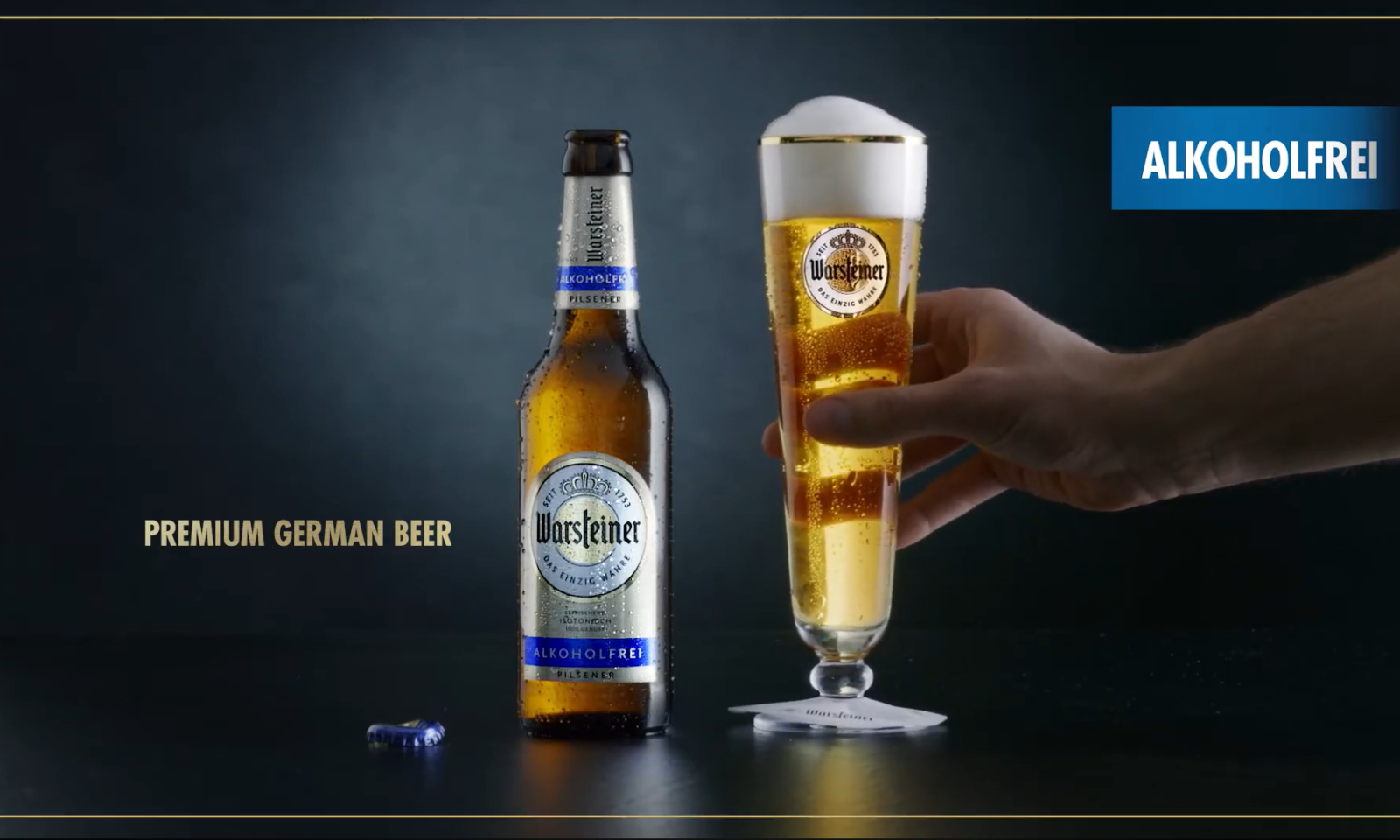 Twee Warsteiner pilsener bierglazen, een fles en een hand tegen een donkere achtergrond.