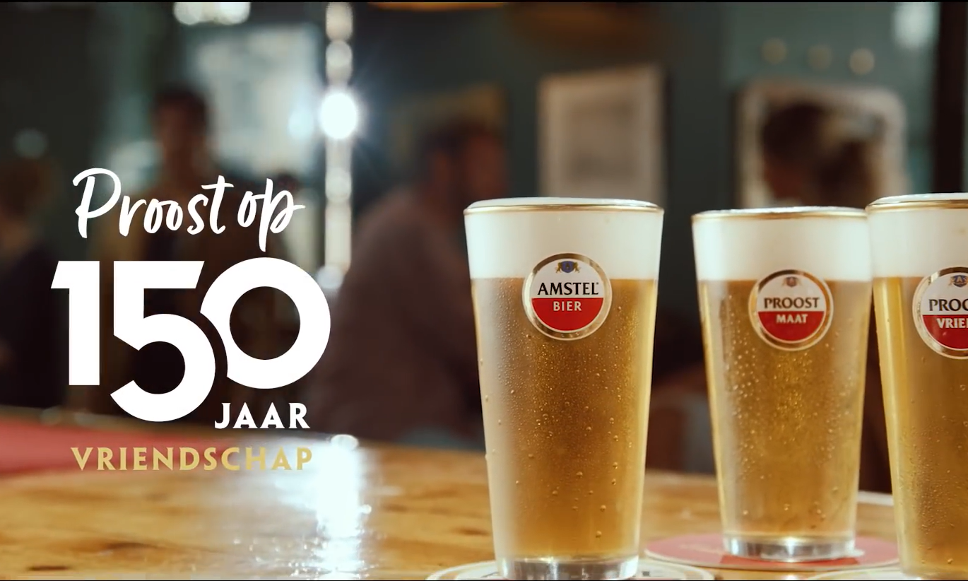 Drie Amstel bierglazen op een bar met tekst 'Proost op 150 jaar vriendschap'.