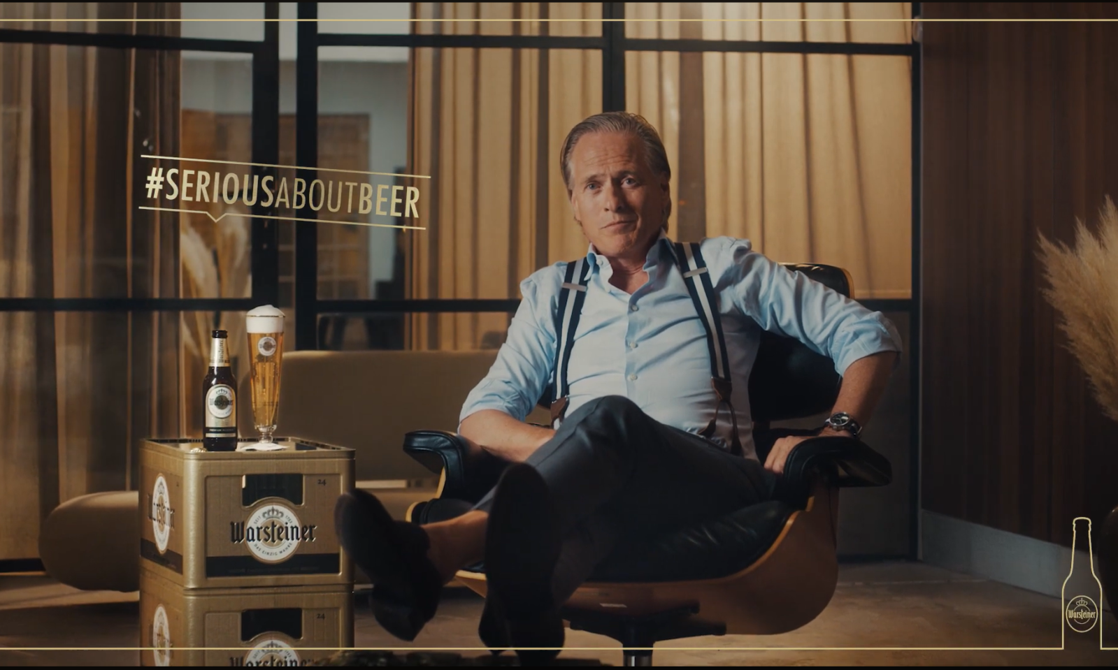 Man in een moderne kamer zittend in een stoel met Warsteiner bier op een krat naast hem.