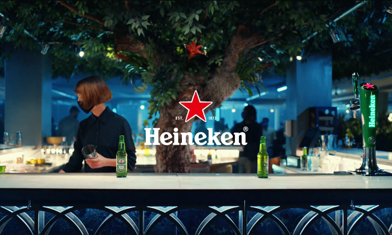 Barkeeper in bar met groene Heineken flesjes en centrale boom
