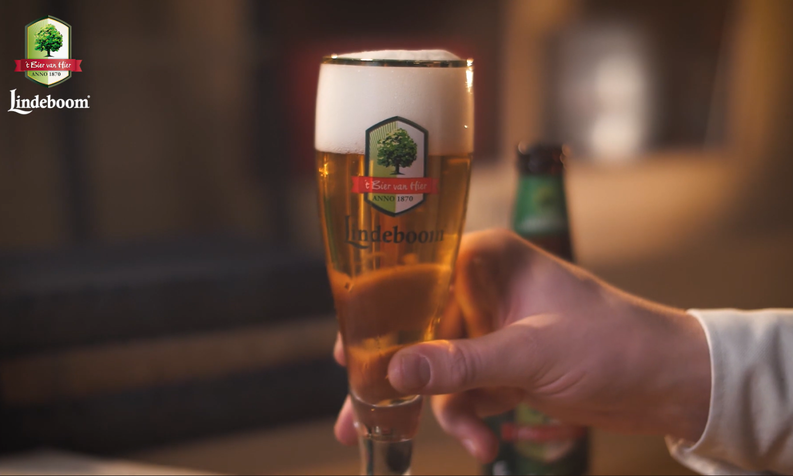 Hand houdt een glas Lindeboom bier gevuld met schuim.