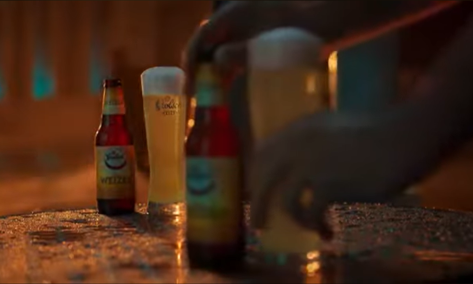 Grolsch witbier in flesjes en glazen op een natte tafel in warme verlichting.