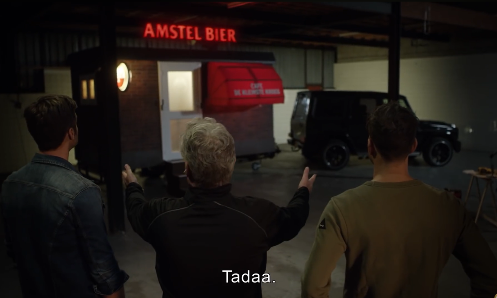 Drie mannen kijken naar een kleine bar met Amstel Bier neonlicht en rode luifel.