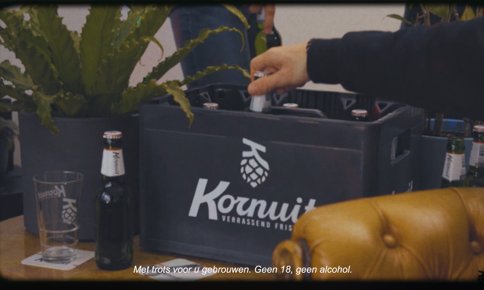 Hand die een Kornuit flesje in een krat plaatst naast een glas en plant.