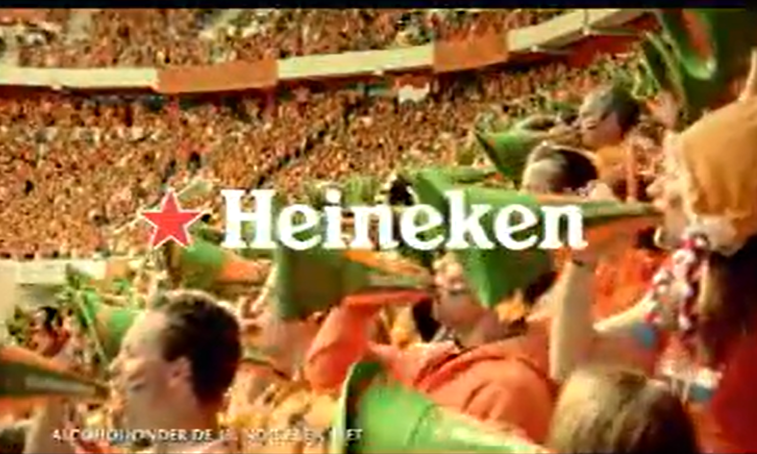 Oranje voetbal fans met groene hoeden en Heineken logo in stadion.