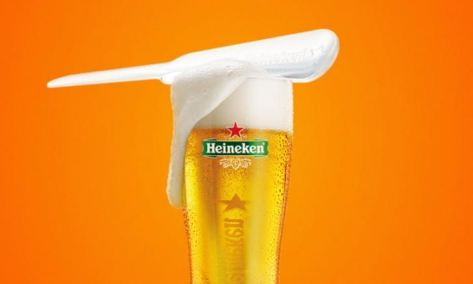 Heineken glas met schuim en een oranje achtergrond.