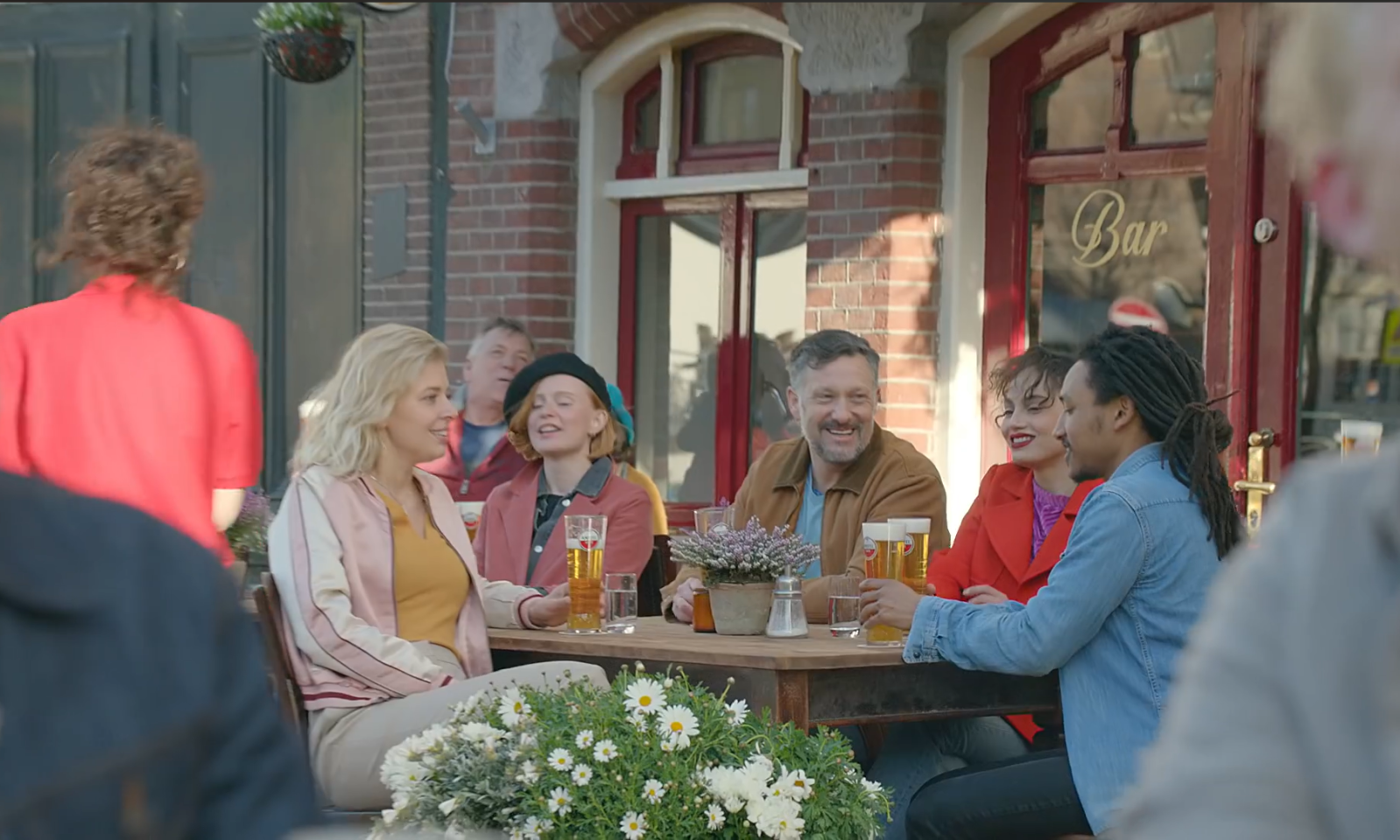 Groep mensen lachend en bier drinkend op een terrasje bij een bar in Amsterdam.