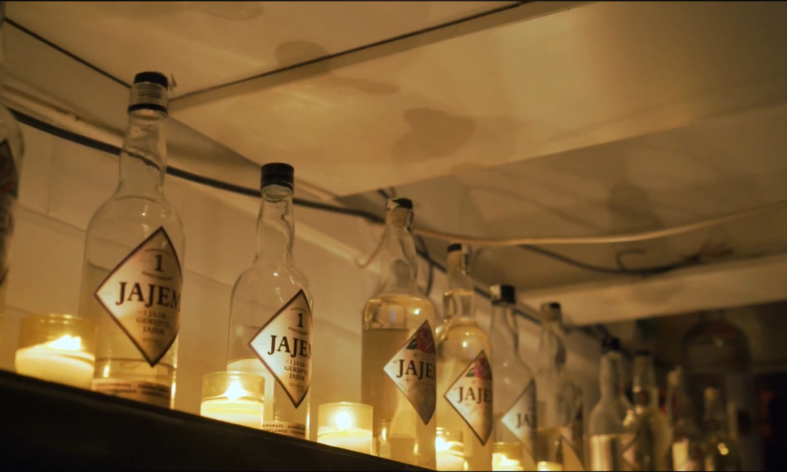 Planken met flessen Jajem en brandende kaarsen in een sfeervol verlichte ruimte.