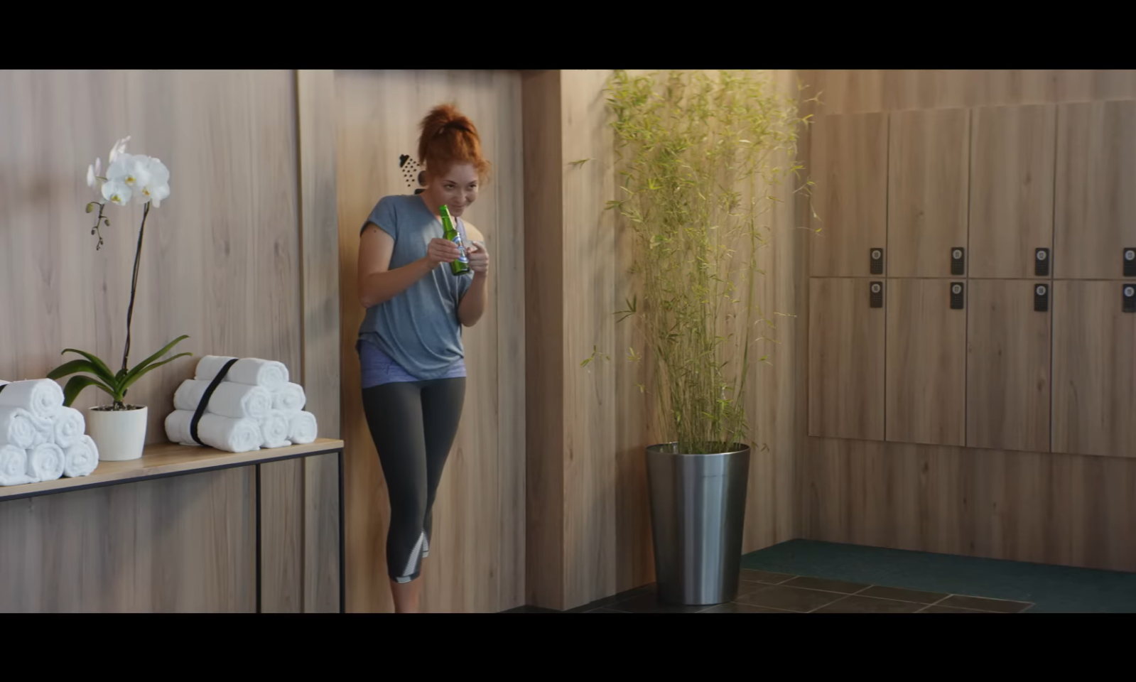 Vrouw in een sportieve outfit opent een flesje in een moderne kleedkamer.