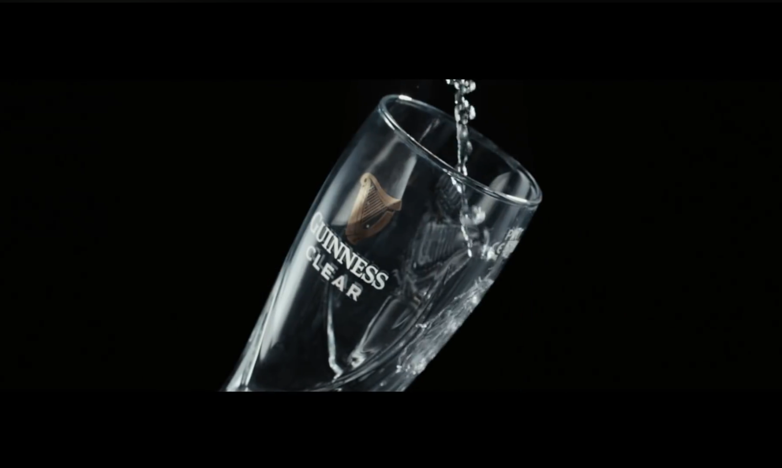 Glas Guinness Clear wordt gevuld met water tegen een zwarte achtergrond.