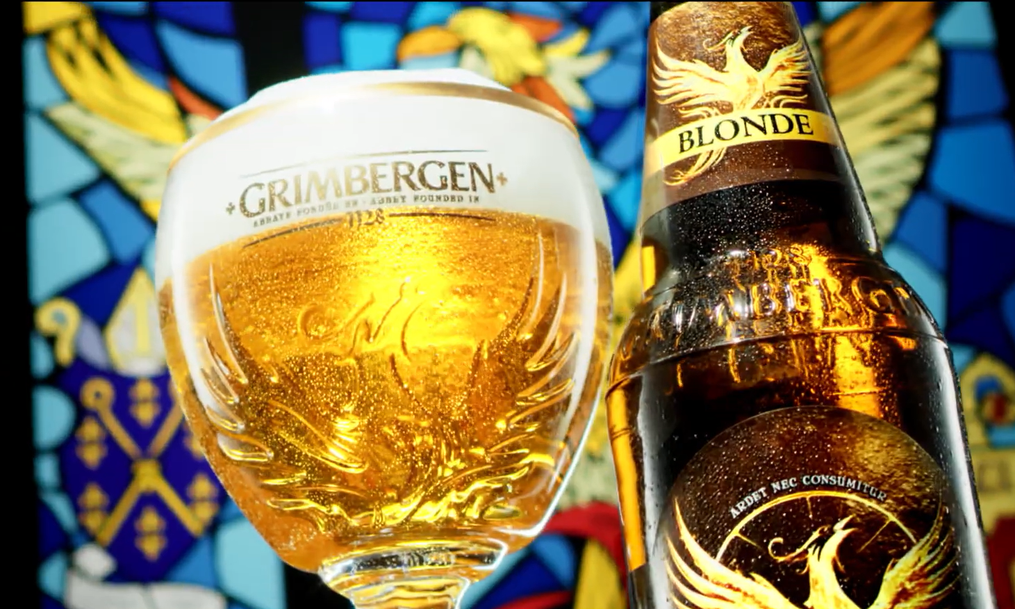 Glas en fles Grimbergen bier tegen glas-in-lood achtergrond.