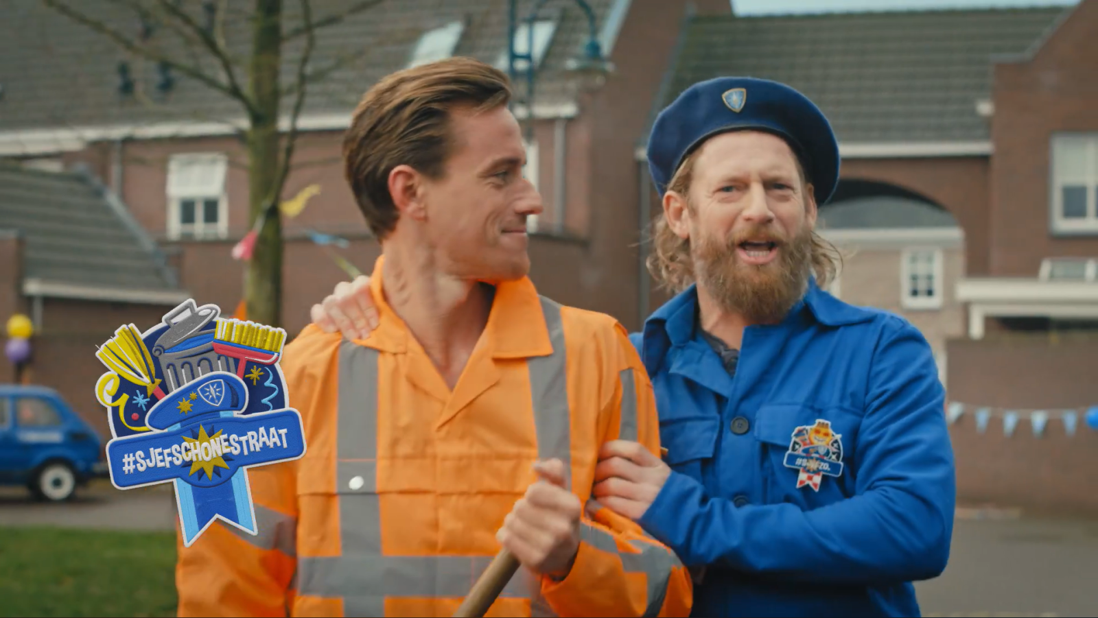 Twee mannen in oranje en blauwe overalls bij carnaval met logo 
