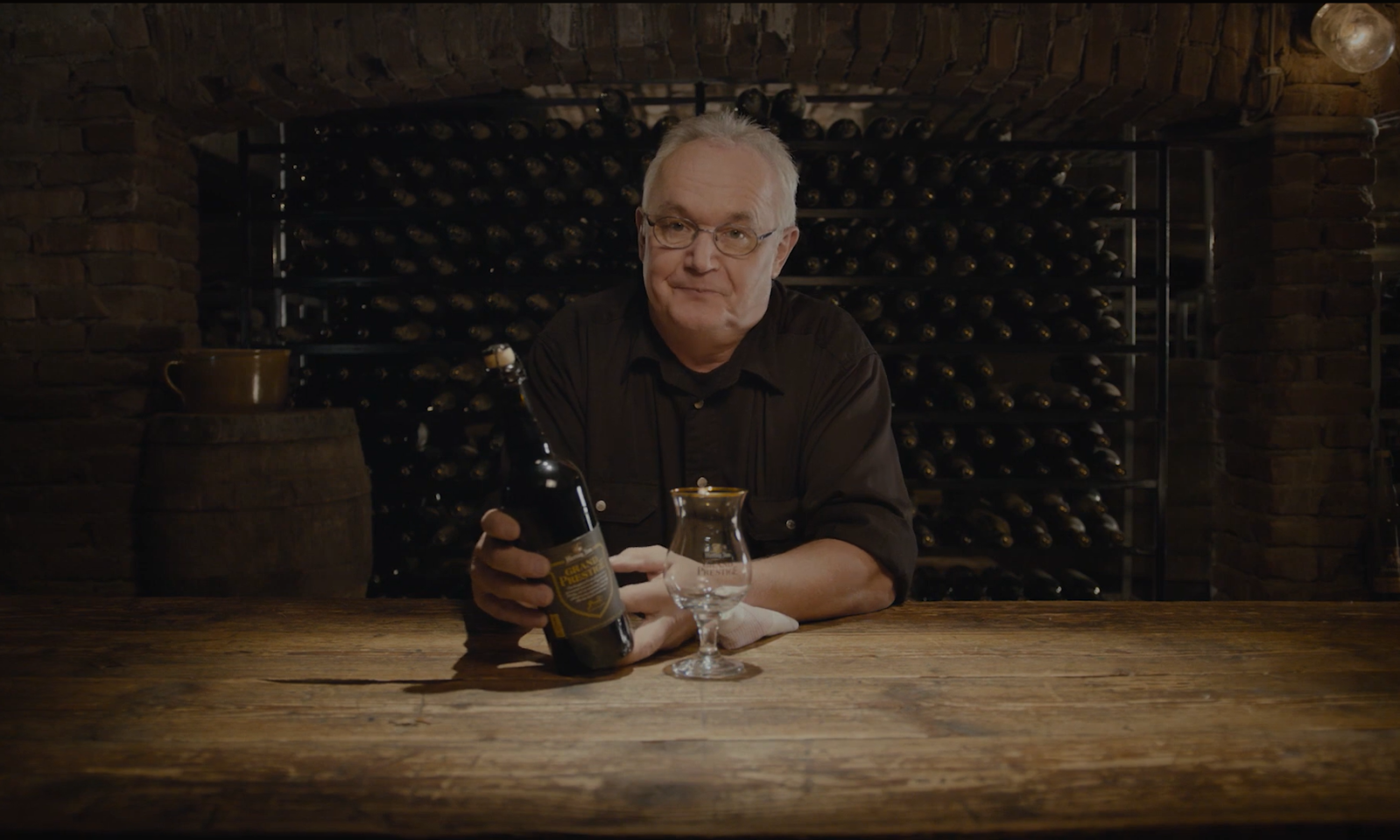 Man houdt een fles Hertog Jan Grand Prestige vast in een wijnkelder.