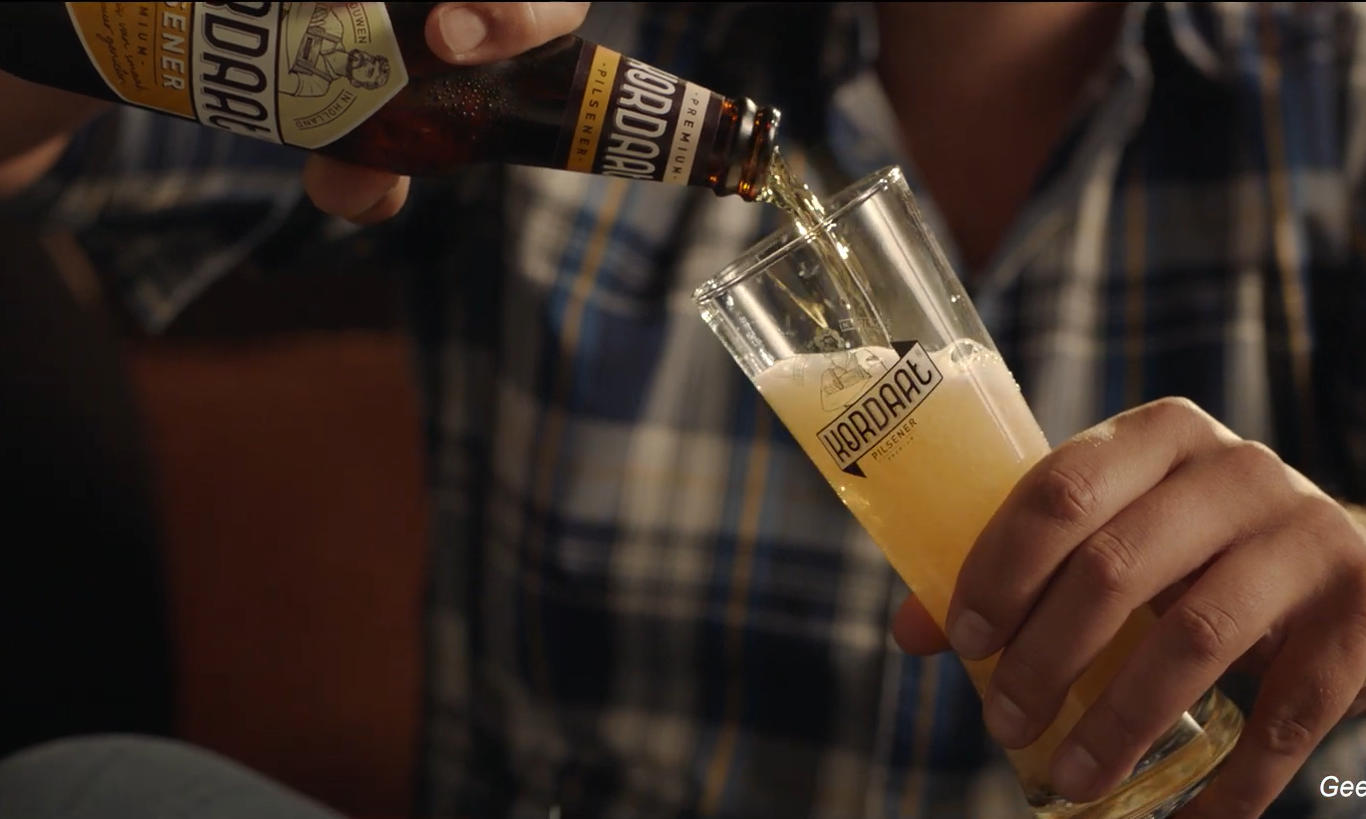 Iemand schenkt een fles Kordaat pilsener in een glas.