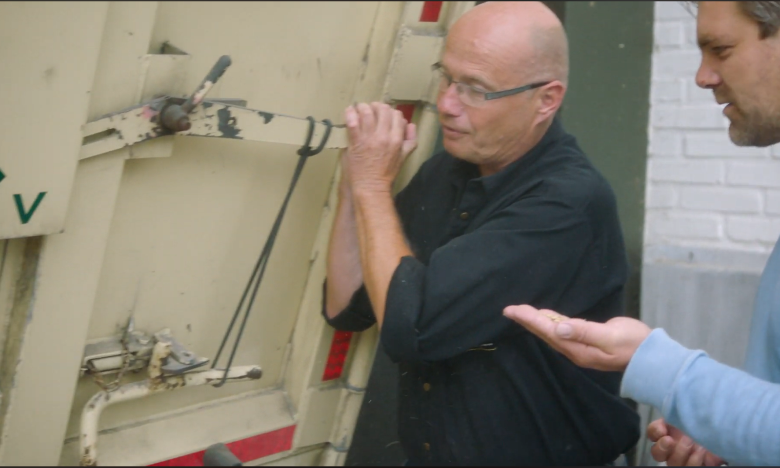 Twee mannen bespreken iets naast een stuk landbouwmachine.