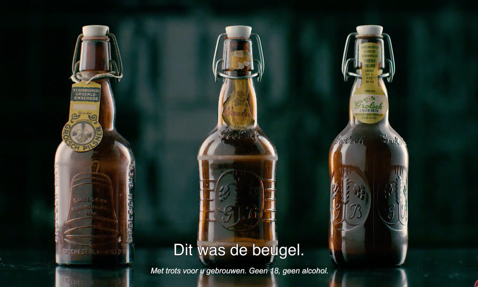 Drie bruine Grolsch beugelflessen met verschillende etiketten op een donkere achtergrond.