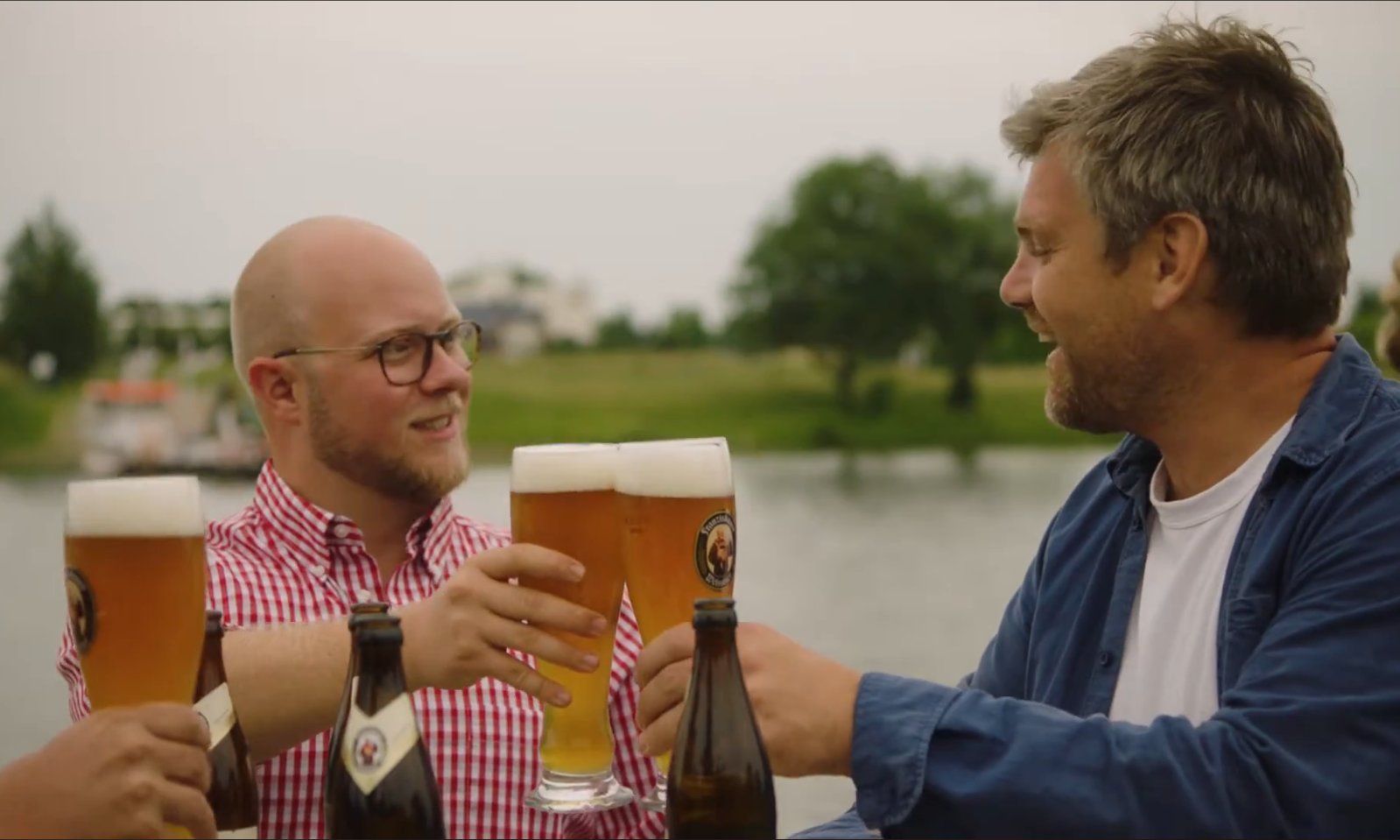 Twee mannen proosten met glazen bier aan de waterkant.