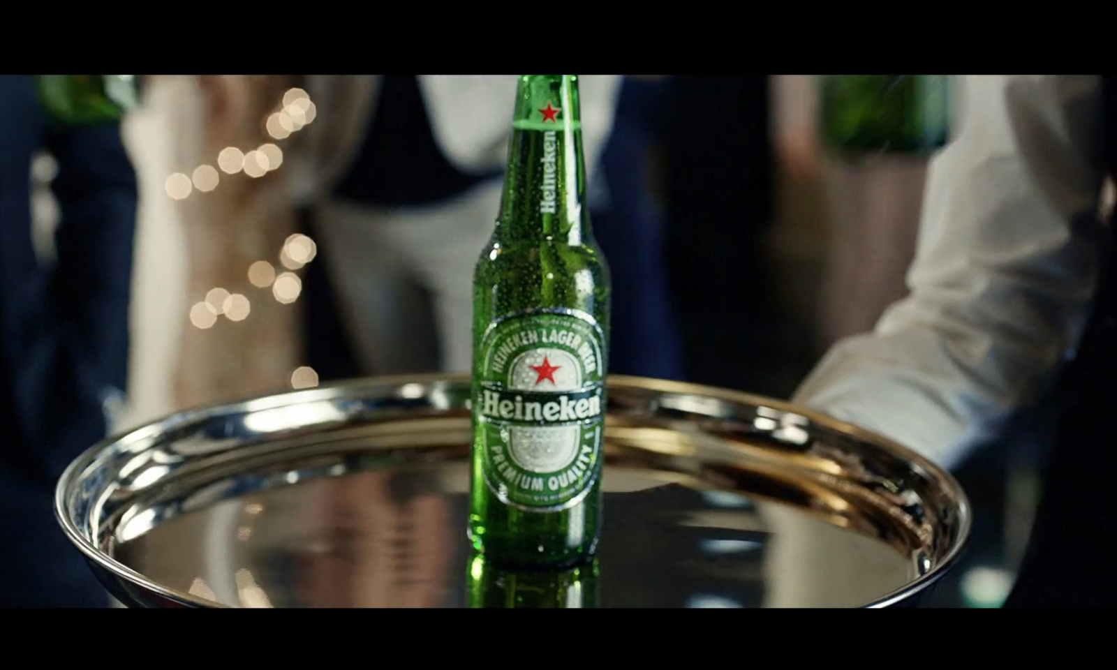 Een fles Heineken bier op een dienblad in een chique omgeving met feestverlichting.