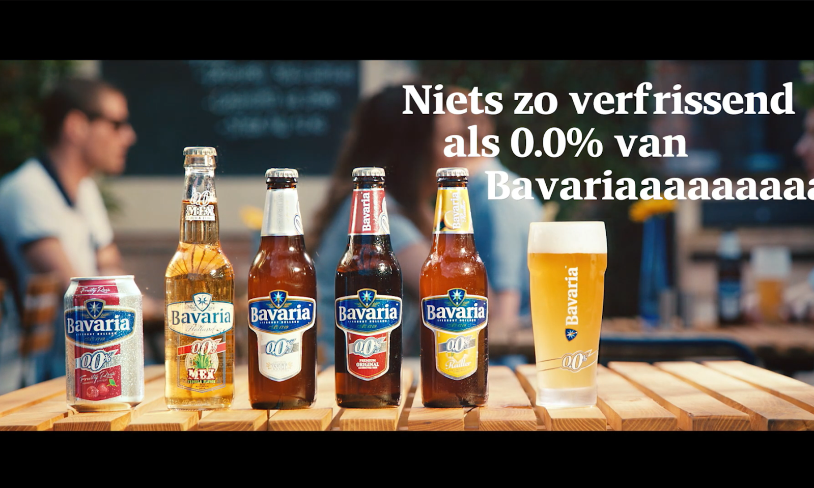Bavaria 0.0% bieren op een houten tafel, met mensen op de achtergrond.