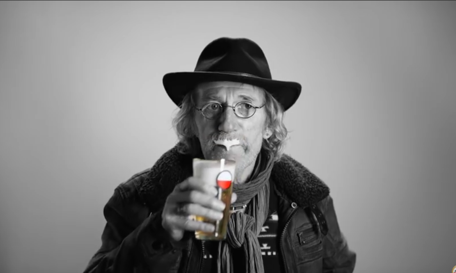 Man met hoed en bril drinkt bier en heeft een schuimsnor, Amstelglas zichtbaar.