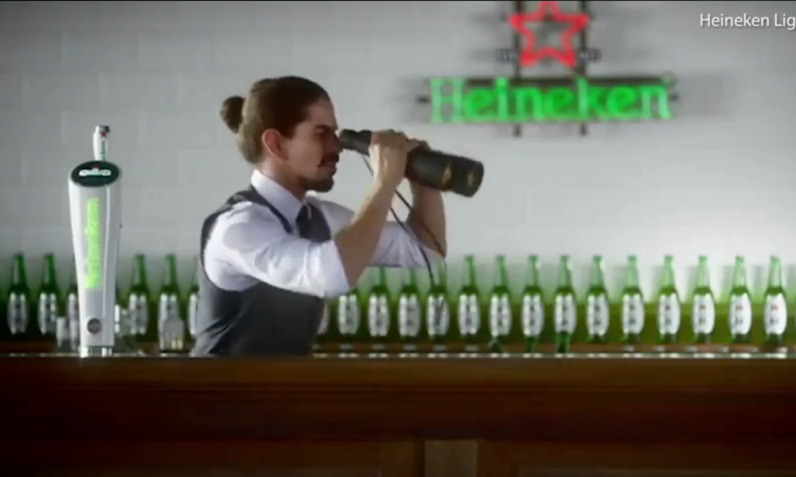 Barman met verrekijker in een bar met Heineken logo op de achtergrond.