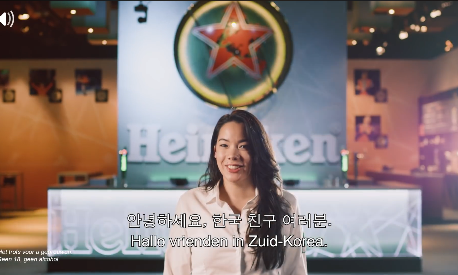 Vrouw in witte blouse, staand voor Heineken-logo met teksten in het Koreaans en Nederlands.