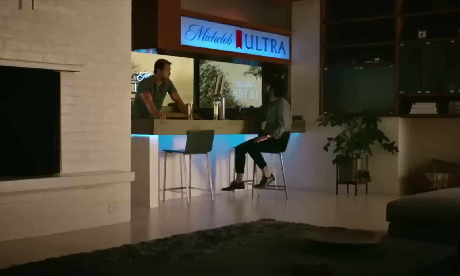 Twee mensen bij een bar met een Michelob Ultra logo en lichte gloed.