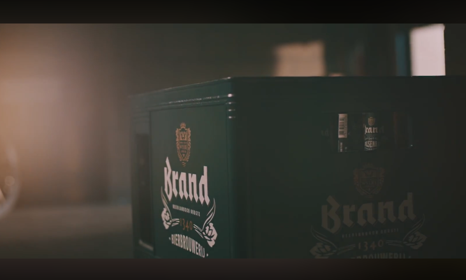 Donkere bierkratten met het Brand-logo in een schuur met fietswiel op de achtergrond.