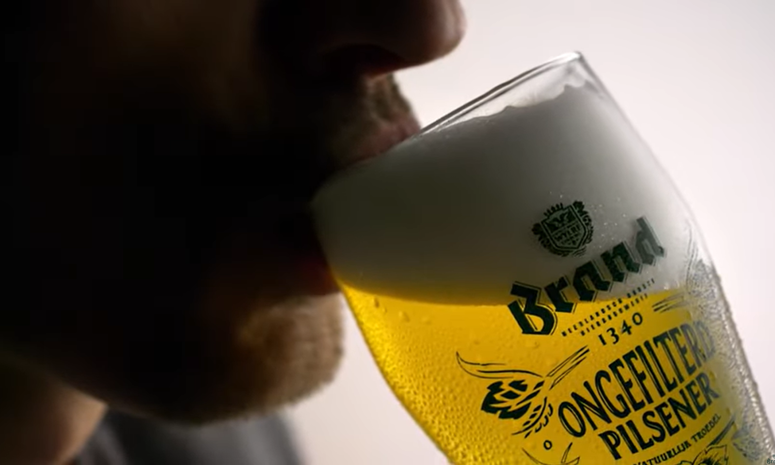 Man drinkt uit een glas Brand Ongefilterd Pilsener met schuimkraag.