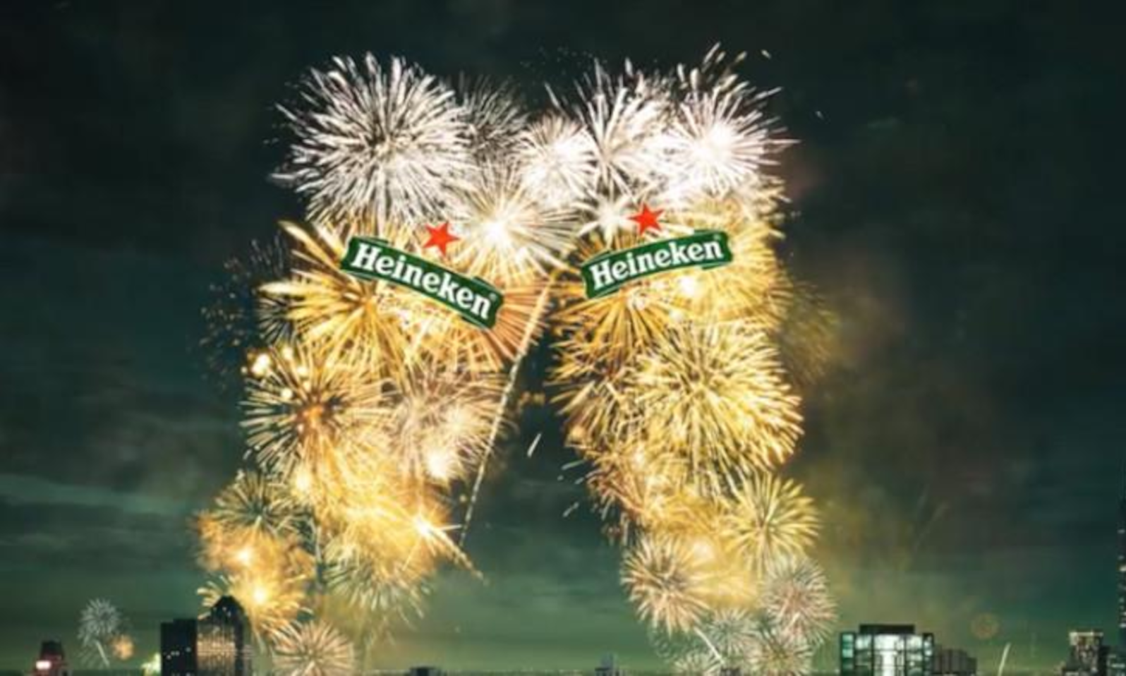 Grote vuurwerkshow boven een stad met een Heineken-thema en nachtelijke hemel.