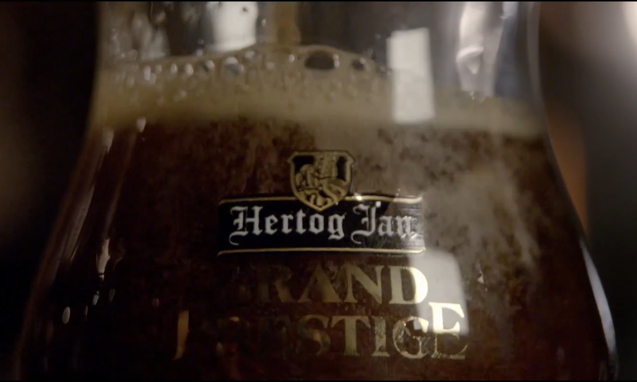 Close-up van een glas donker Hertog Jan bier met logo.