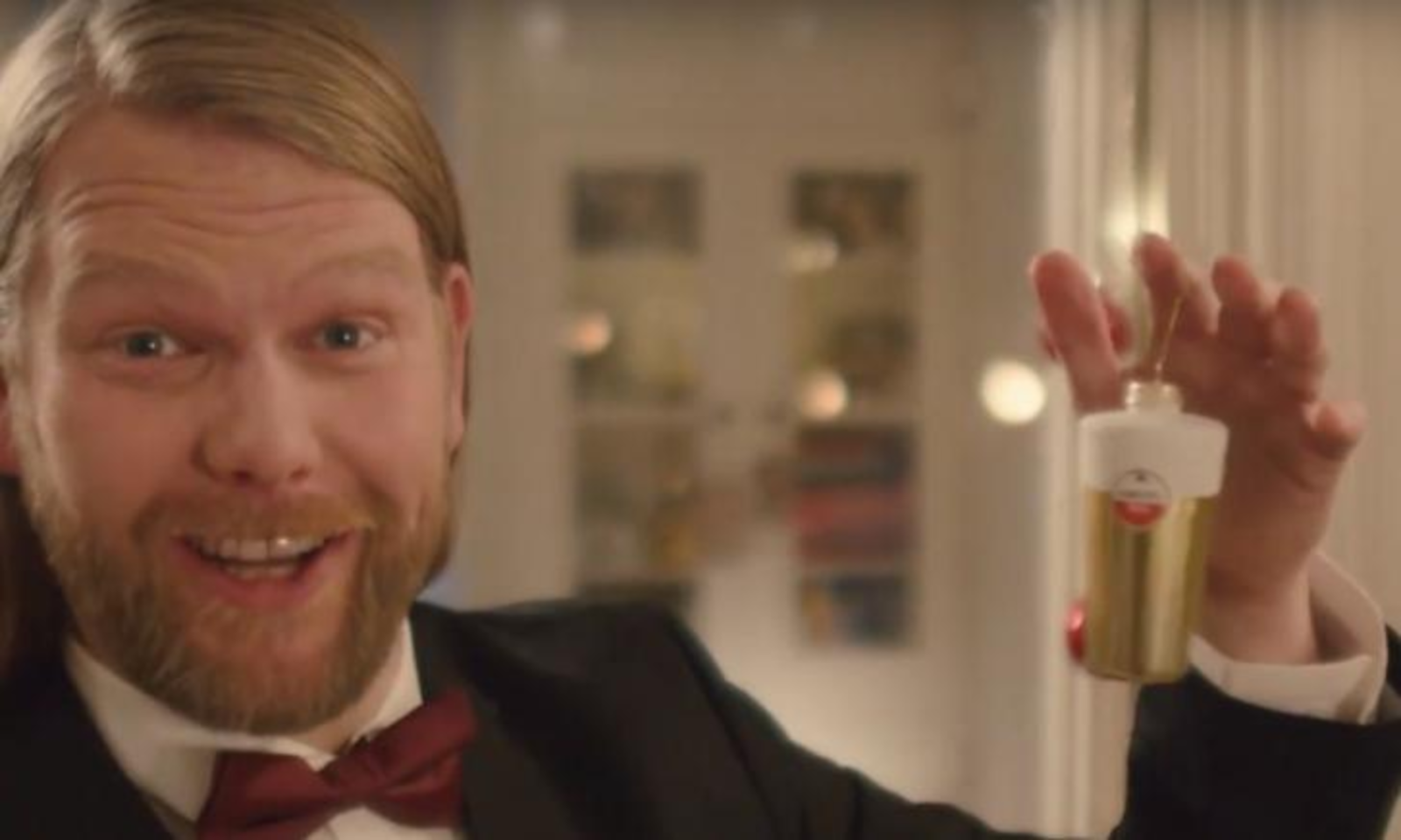 Man in smoking houdt een Amstel kerstornament omhoog met een glimlach.