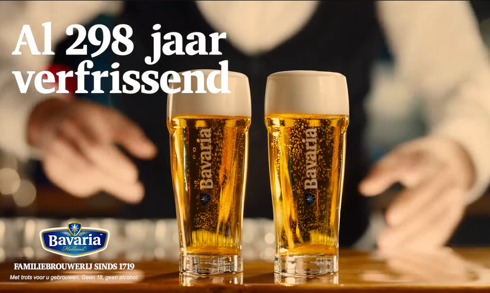 Twee glazen bier met schuimkraag op een houten bar, handen op de achtergrond.