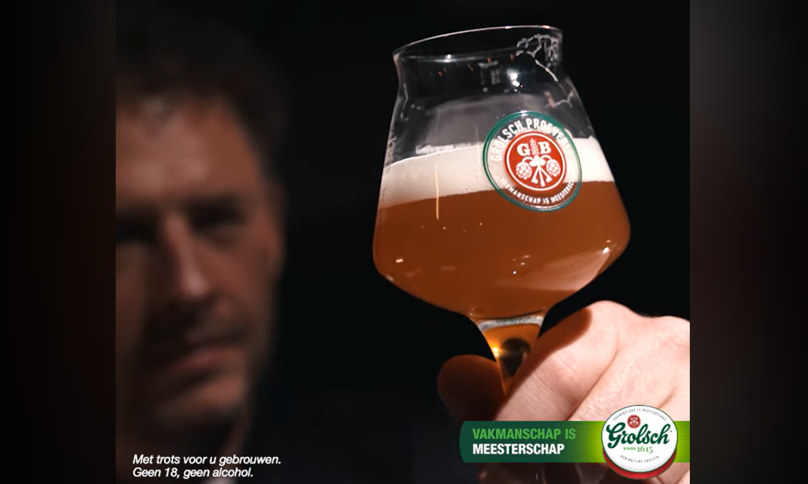 Man houdt een glas Grolsch bier omhoog in gedimde verlichting.