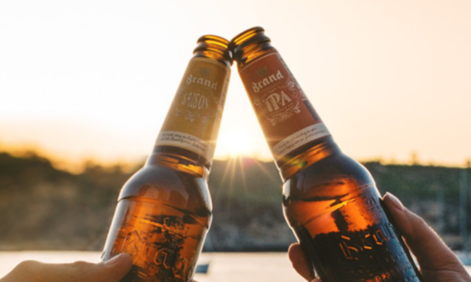 Twee bierflesjes klinken met een zonsondergang op de achtergrond.
