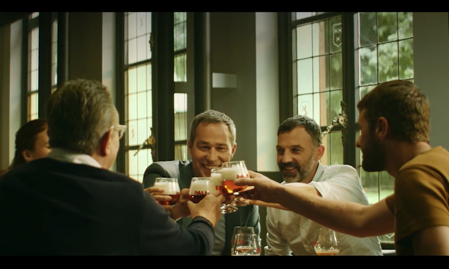 Groep mannen die proosten met glazen bier in een café, lachend en vrolijk.