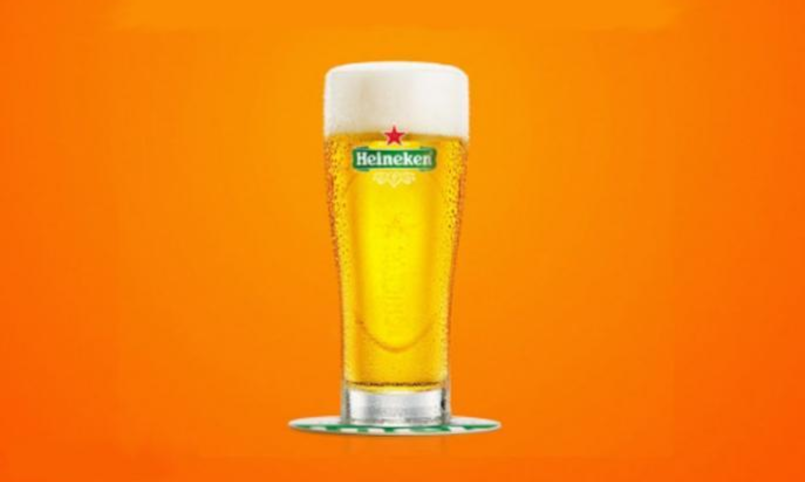 Een Heineken glas gevuld met bier tegen een oranje achtergrond.