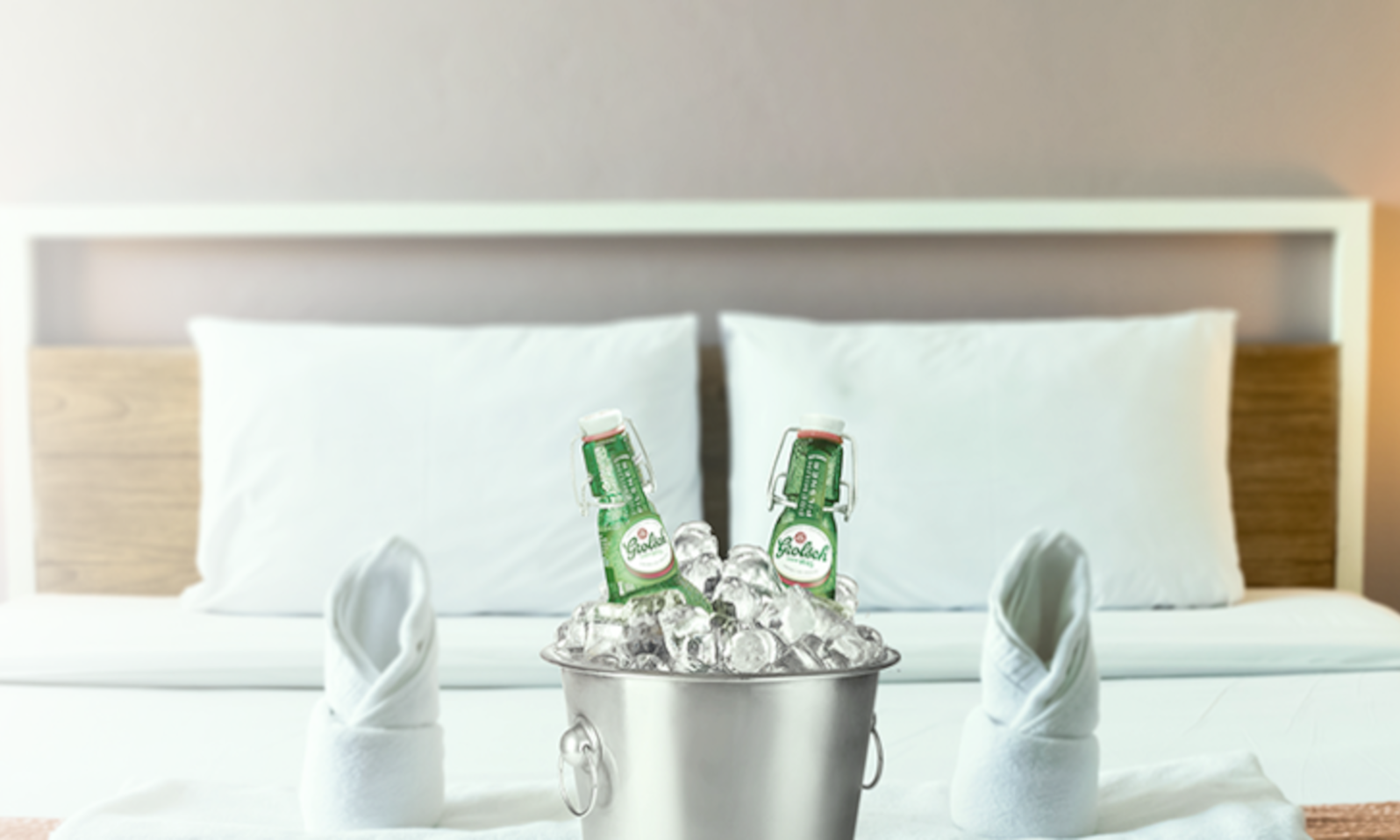 Twee bierflesjes in een ijsemmer op een hotelbed met witte kussens en opgevouwen handdoeken.
