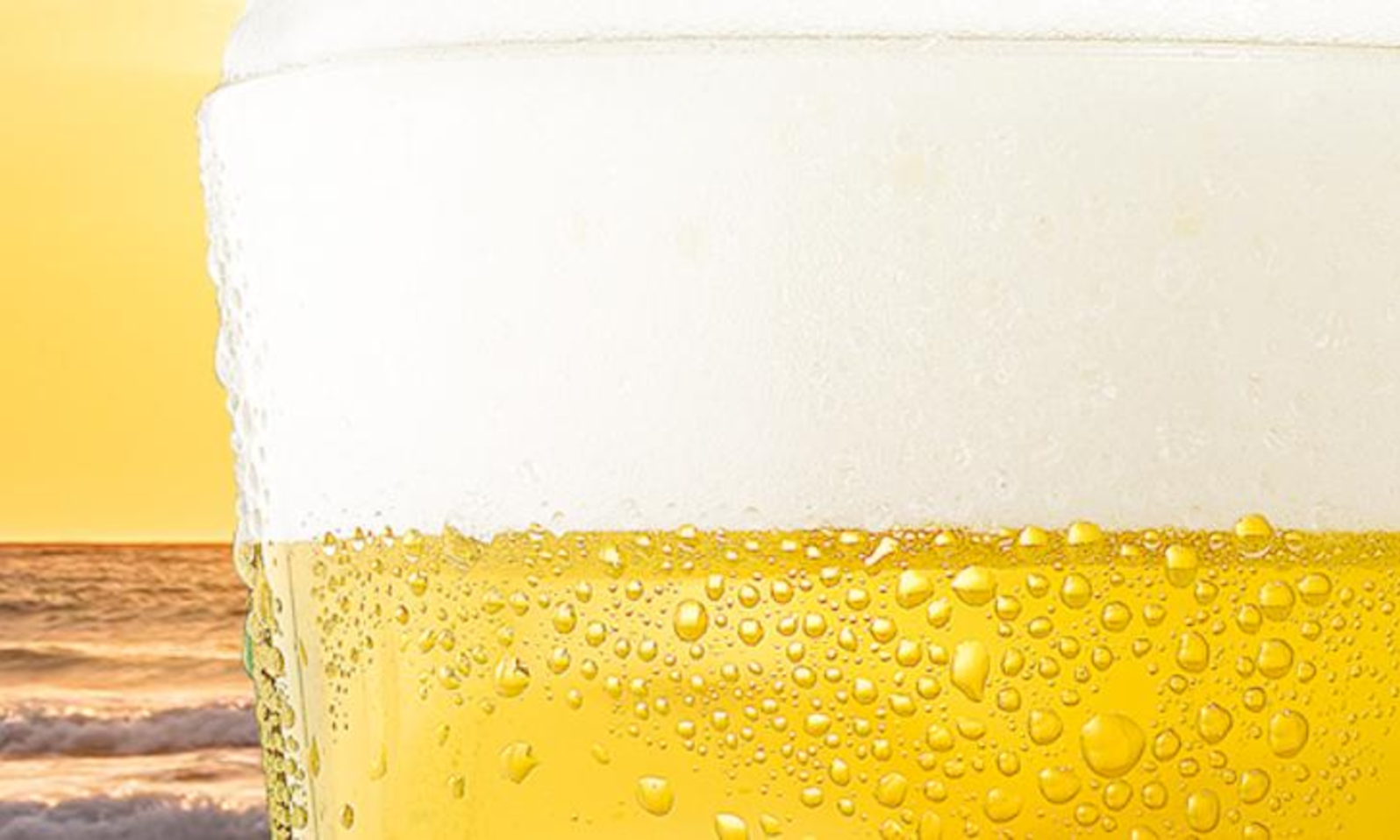 Glas bier met schuimkraag tegen een zonsondergang boven de oceaan.