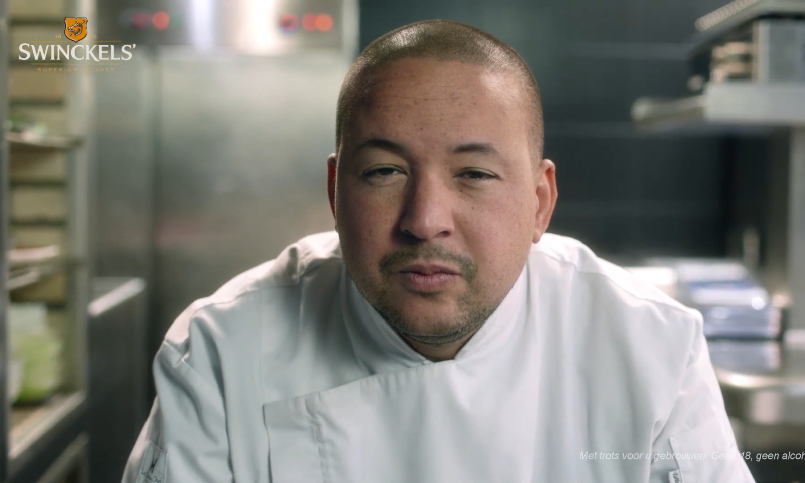 Man in witte chefkoksjas in professionele keuken kijkt in camera.