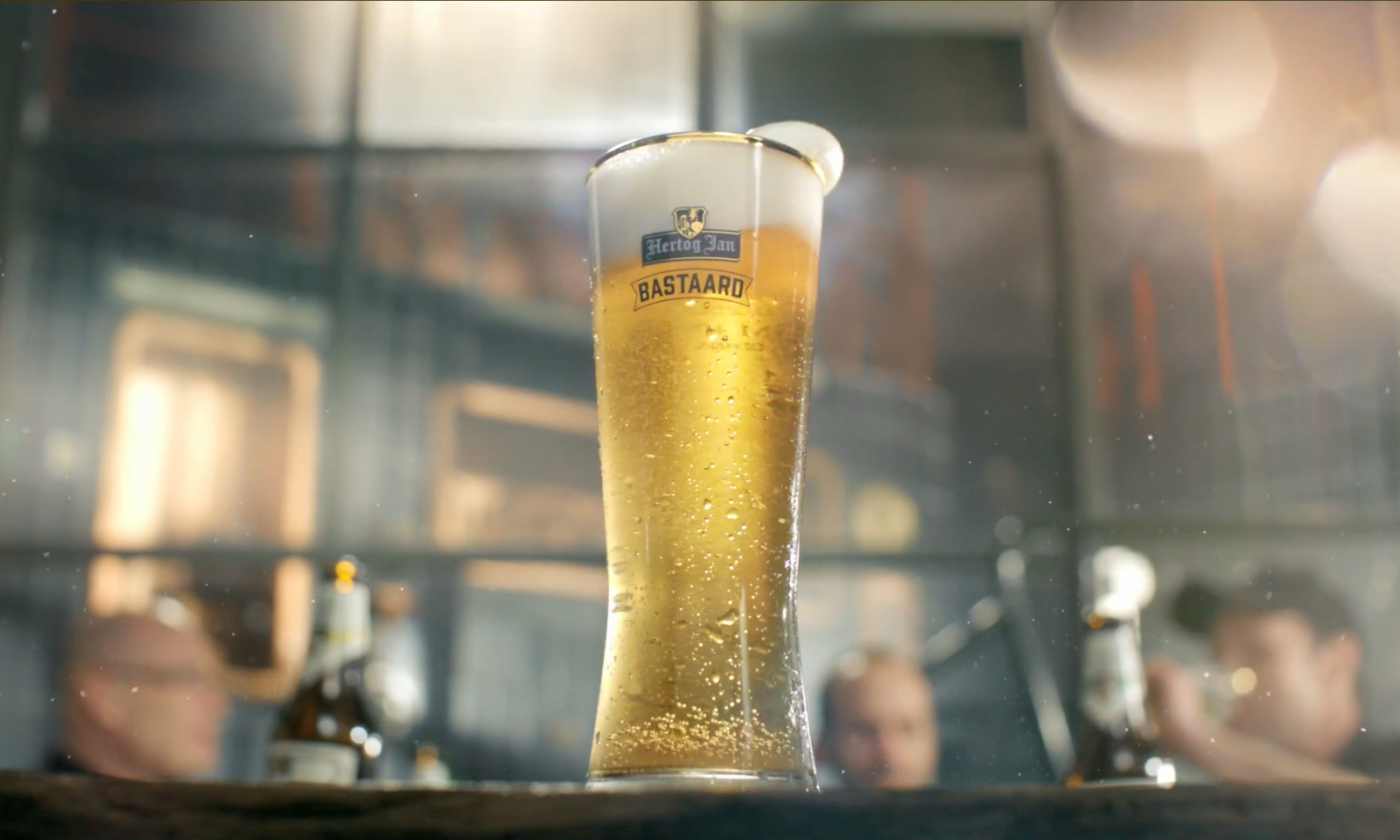 Close-up van een glas Hertog Jan Bastaard bier op een bar met onscherpe achtergrond.
