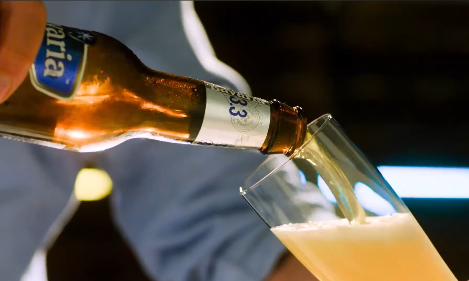 Een flesje bier wordt in een glas geschonken tegen een wazige achtergrond.