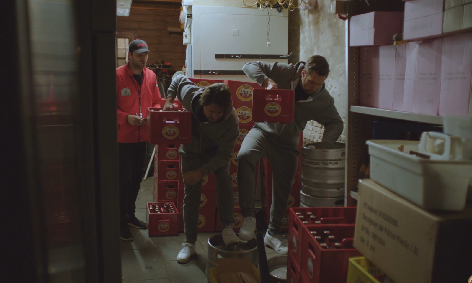 Drie mannen verplaatsen bierkratten en vaten in een opslagruimte.