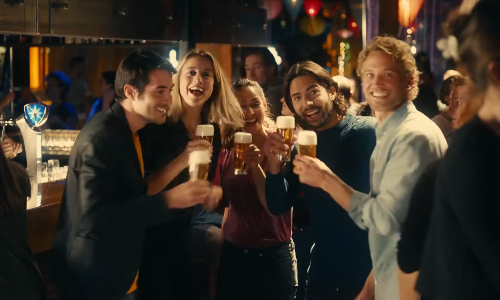 Groep vrienden die proostend bierglazen vasthouden in een drukke bar.