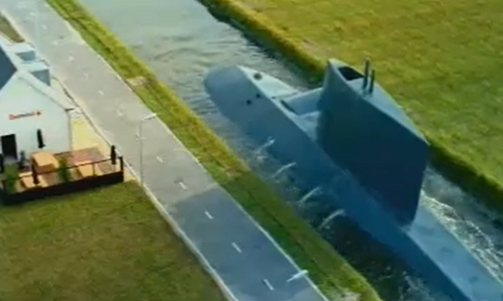 Duikboot varend door een smal kanaal naast een gebouw en een weg.