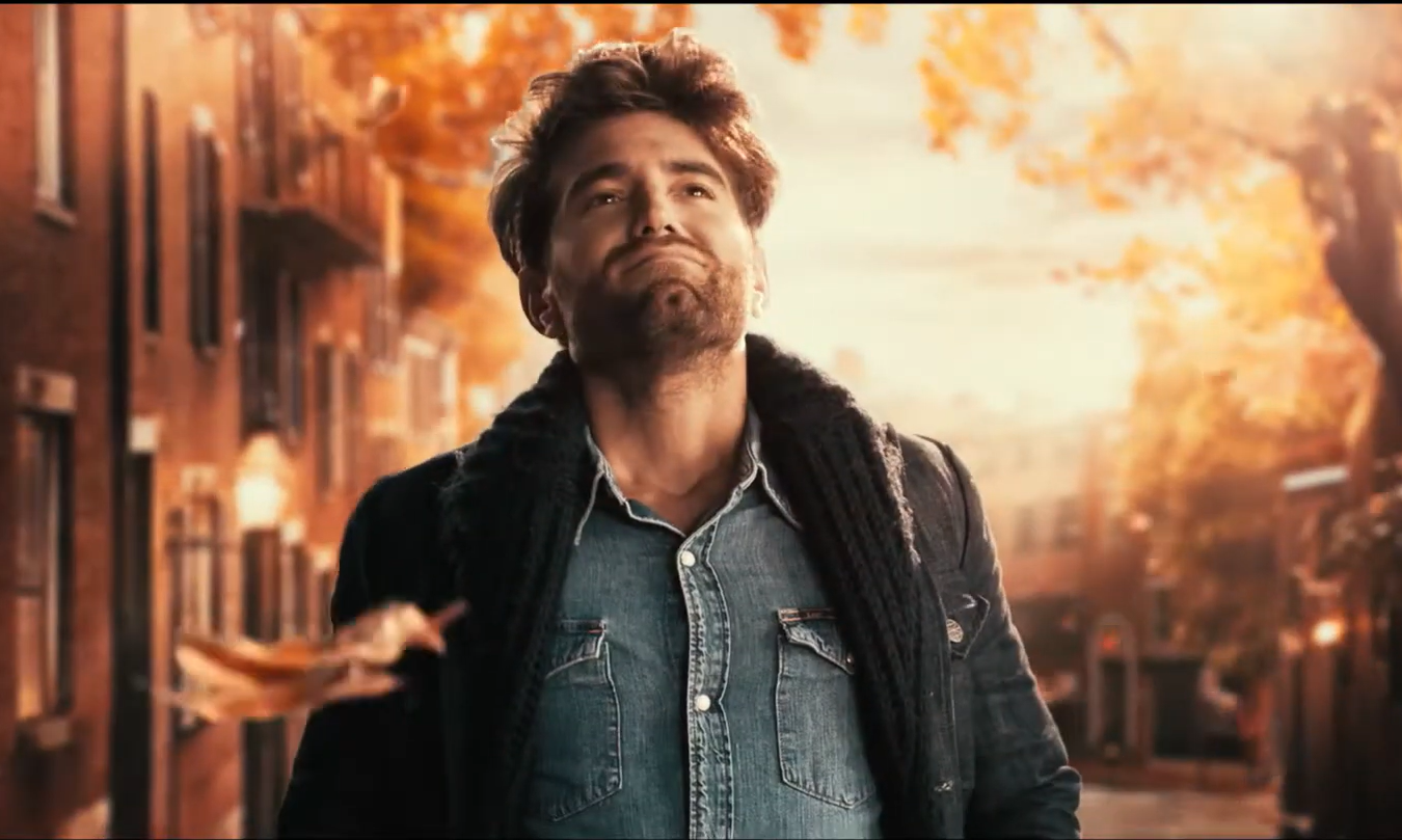 Man geniet van herfstsfeer in een straat met oranje bladeren en bakstenen gebouwen.