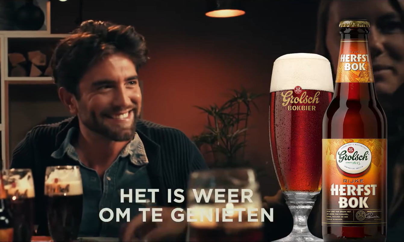 Mensen lachen met Grolsch herfstbokbier op tafel in een warme setting.